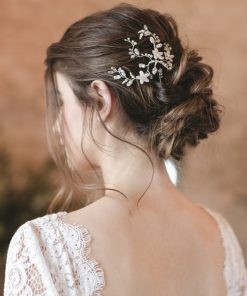 Bride in a barn with stone wall behind. She looks away, showing her hair in a low undone bun wearing a Small hair up wedding hair vine. Her gown has a low back and is covered in lace.