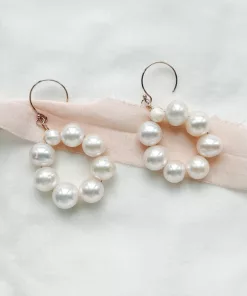 large pearl circle wedding earrings laying on blush pink silk ribbon, and an ivory fabric.