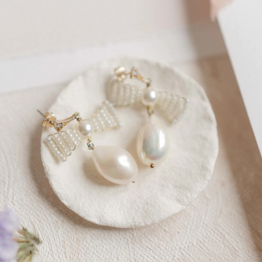 Bow bridal earrings with pearls set on a small ivory coloured dish.